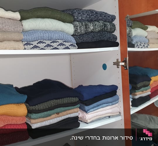 סוודרים מקופלים בארון עץ עם מדפים לבנים